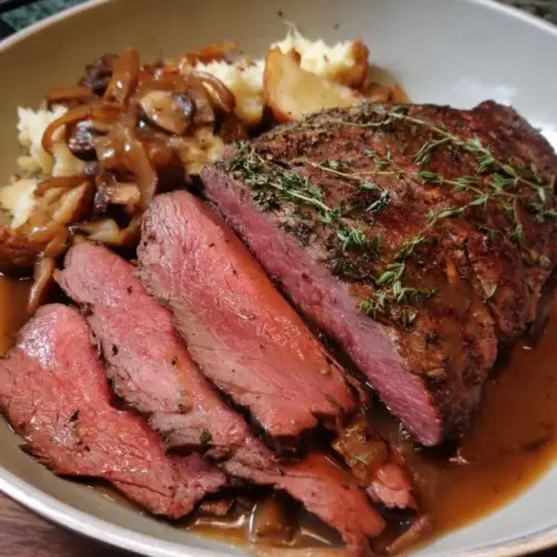 Herb-crusted roast beef served with pan gravy on a rustic wooden table