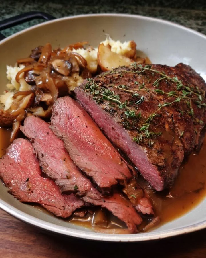 Herb-crusted roast beef served with pan gravy on a rustic wooden table